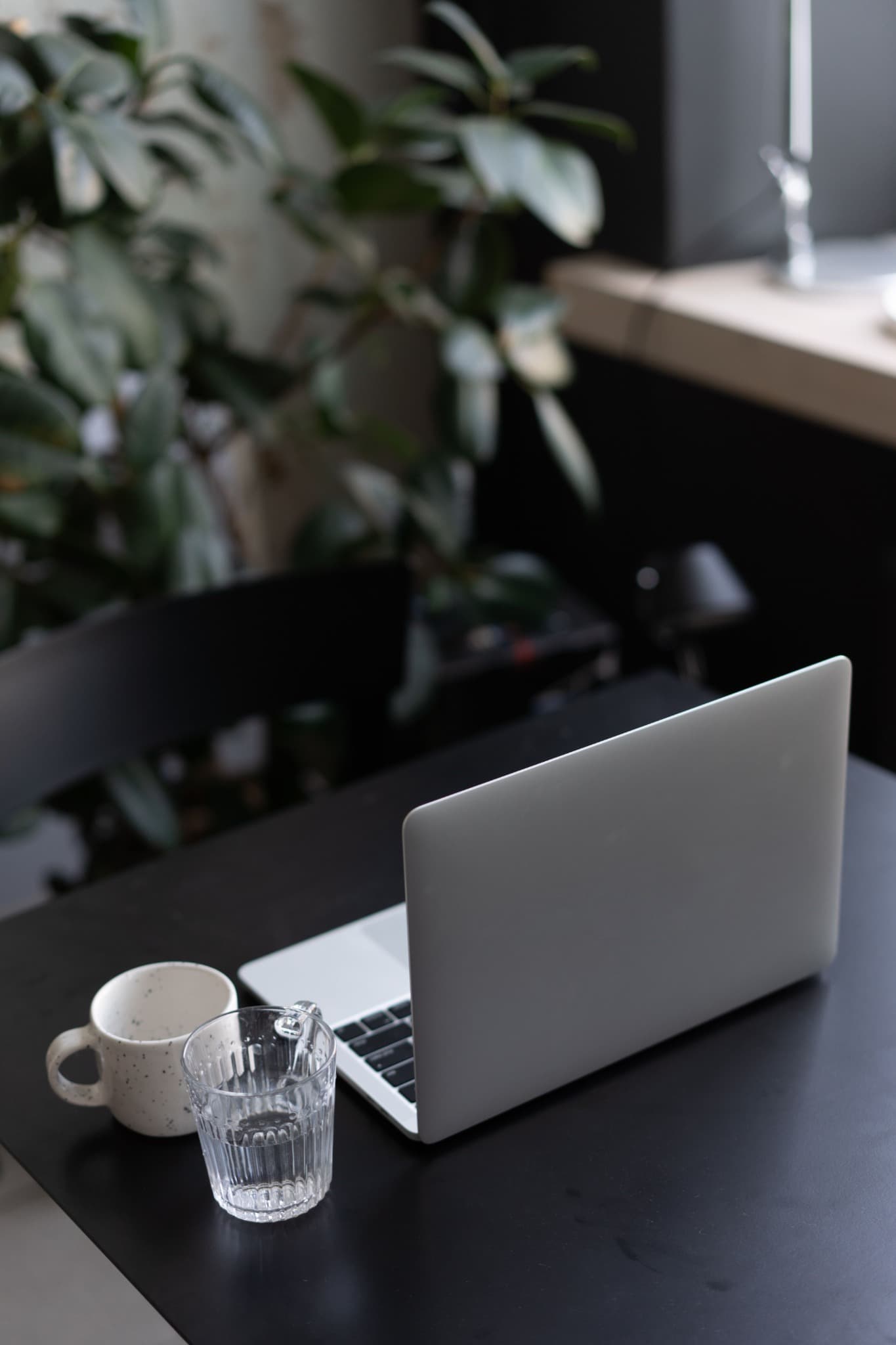 A bright minimal desk by a window with a laptop, two cups and small plants, photographed in natural light.